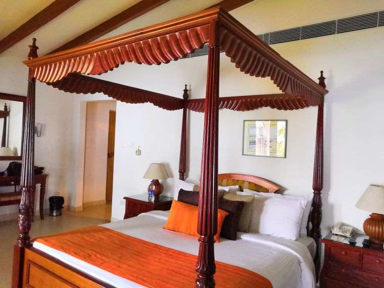 Inside our beautiful Lake-side cottage in Alleppey. There is a wooden bed with four poles, typical of Kerala-style, lamps and lovely aesthetics.