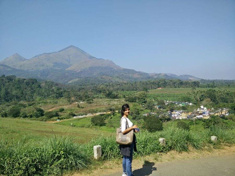 Sinjana standing on the road on her way to the Banasura Sagara Dam on a sunny day in Wayanad. The hills at the backdrop look lovely across the azure sky. This is the best place to visit in Wayanad Itinerary