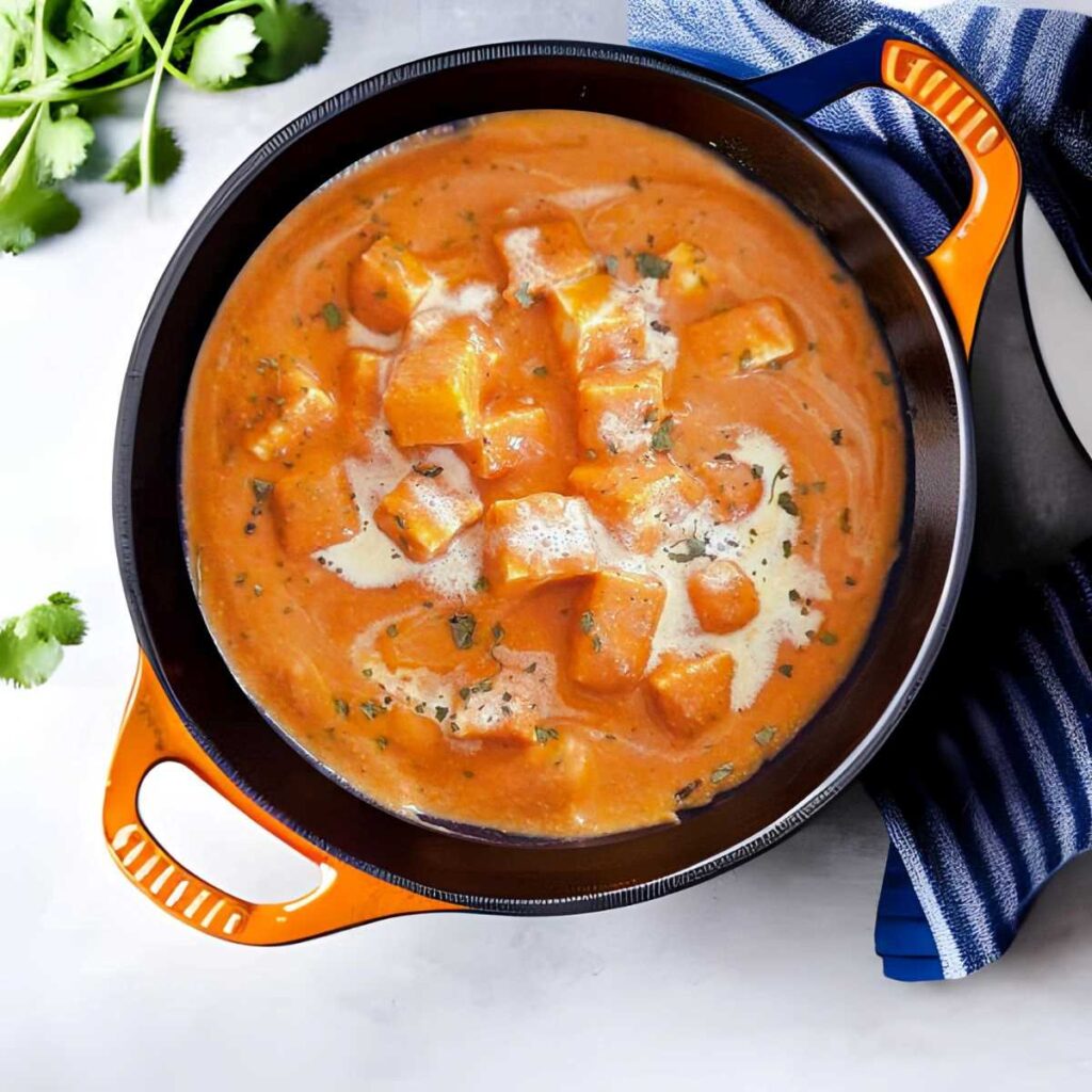 12 Easy Indian Recipes for Beginners 10 image of paneer butter masala in a black bowl with a blue napkin and cilantro off to the side
